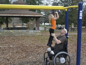Wheel-chair bound amputee military father helping his daughter on the playground
